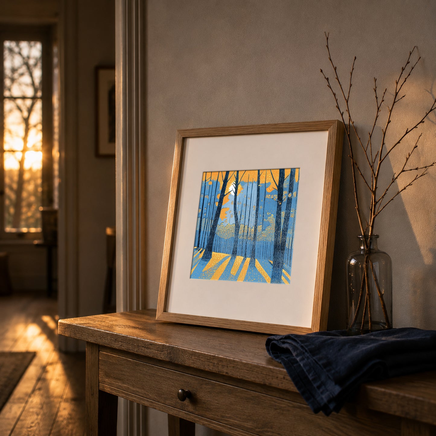 Framed Into the Woodland linocut print displayed on a wooden console in a warm interior with low natural light.