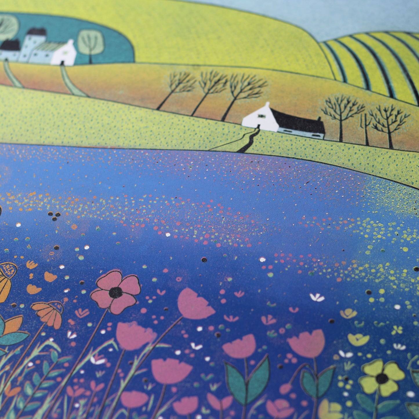 Close-up of the Sea of Tranquility linocut showing the textured blue meadow and hand-printed pink and yellow flowers.