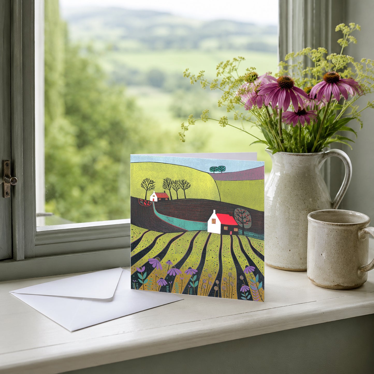 Linocut countryside greeting card displayed on a mantelpiece with dried stems in a pale vase