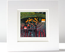 Load image into Gallery viewer,  linocut print titled "Autumn Glow" features a vibrant autumn tree, rolling hills, a white house, and plants in shades of red and grey. A lino cutting tool lies beside the artwork. The edition number and artist's signature are visible below.