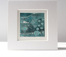 Load image into Gallery viewer, A detailed linocut artwork titled 'Serene Paths' by Layla Khan, featuring a tranquil rural scene with minimalist trees, winding paths, and a farmhouse. The print, in cool blue hues, is framed in a white mount, with a lino cutting tool placed beside it for a touch of the creative process.