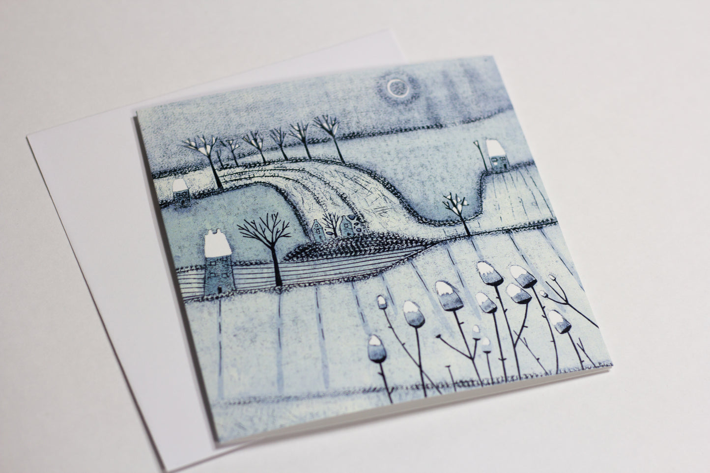 Close-up of a blue-grey winter Christmas card featuring trees, snowy fields and cottages.