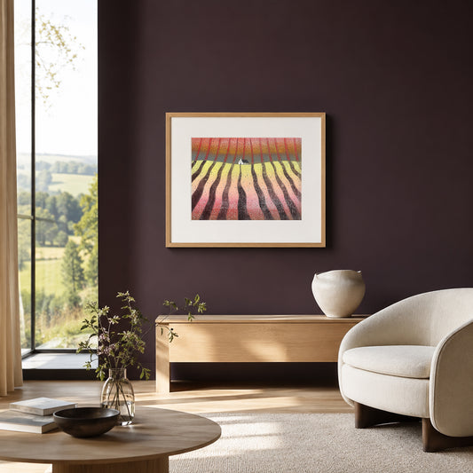 Framed linocut of red furrowed fields on a deep aubergine wall above a light wood console and pale armchair.