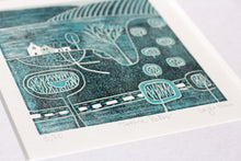 Load image into Gallery viewer, A detailed linocut artwork titled 'Serene Paths' by Layla Khan, featuring a tranquil rural scene with minimalist trees, winding paths, and a farmhouse. The print, in cool blue hues, is framed in a white mount, with a lino cutting tool placed beside it for a touch of the creative process.
