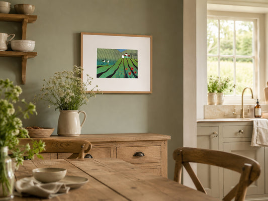 Framed linocut of a green poppy landscape on a sage-green kitchen wall above an oak sideboard with cow parsley.