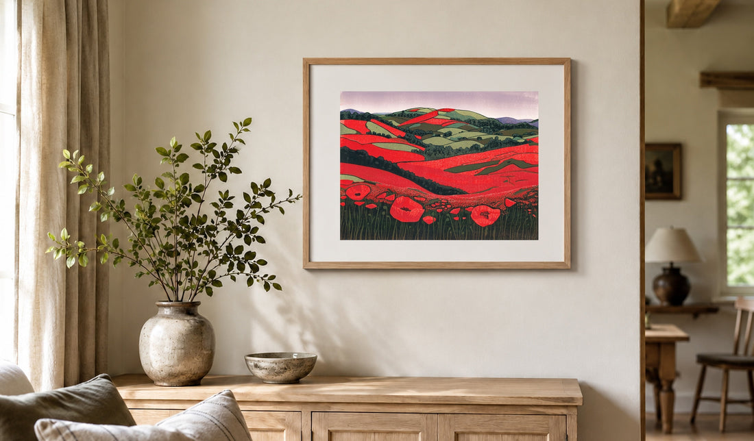 Framed poppy linocut print in a pale oak frame with a white mount above a wooden sideboard.