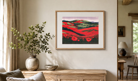 Framed poppy linocut print in a pale oak frame with a white mount above a wooden sideboard.