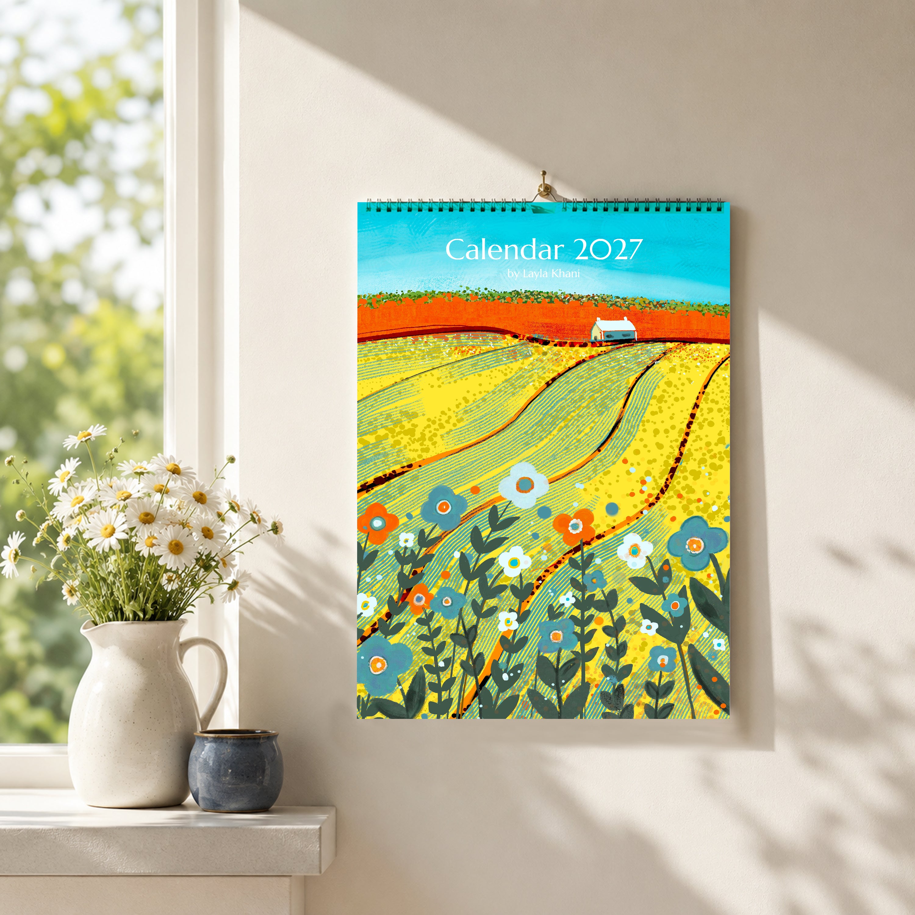 2027 A4 art calendar with colourful countryside painting displayed on a sunlit wall