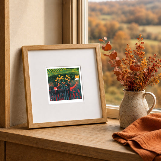 Mini linocut print framed in pale oak, propped on a windowsill with autumn stems in a stone jug