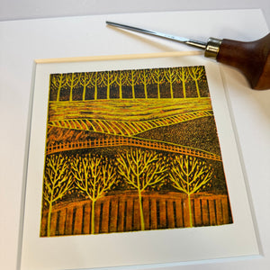 Handcrafted Autumnal Fields mini linocut print featuring autumnal trees and fields in rich golden tones.