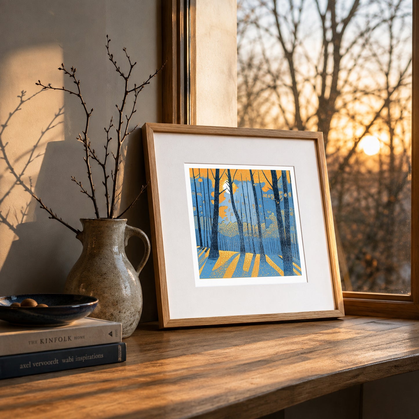 Framed Into the Woodland linocut print displayed on a wooden surface beside a window with warm evening light.