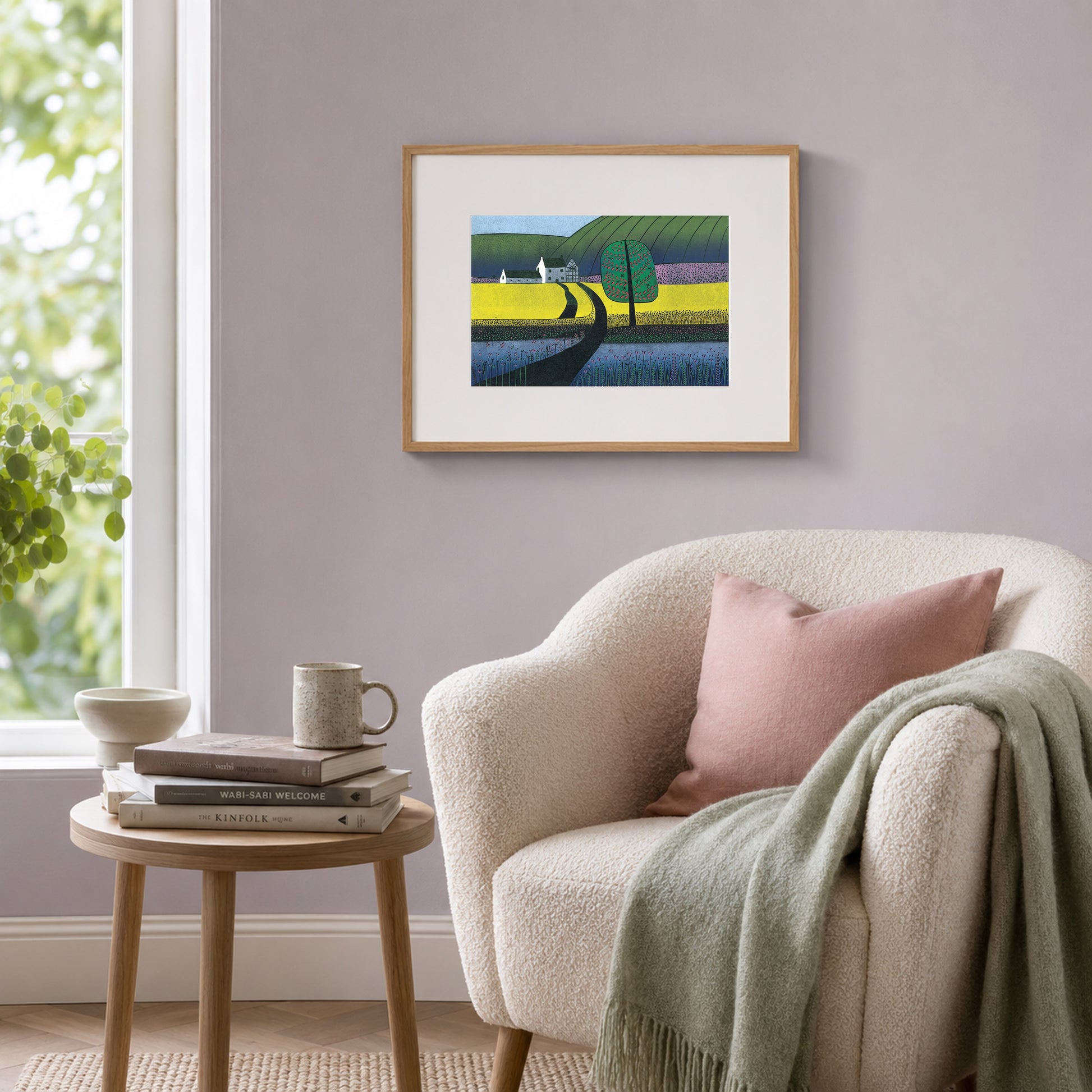 Framed yellow-field landscape print on a lilac-grey wall beside a cream boucle armchair with a sage throw.