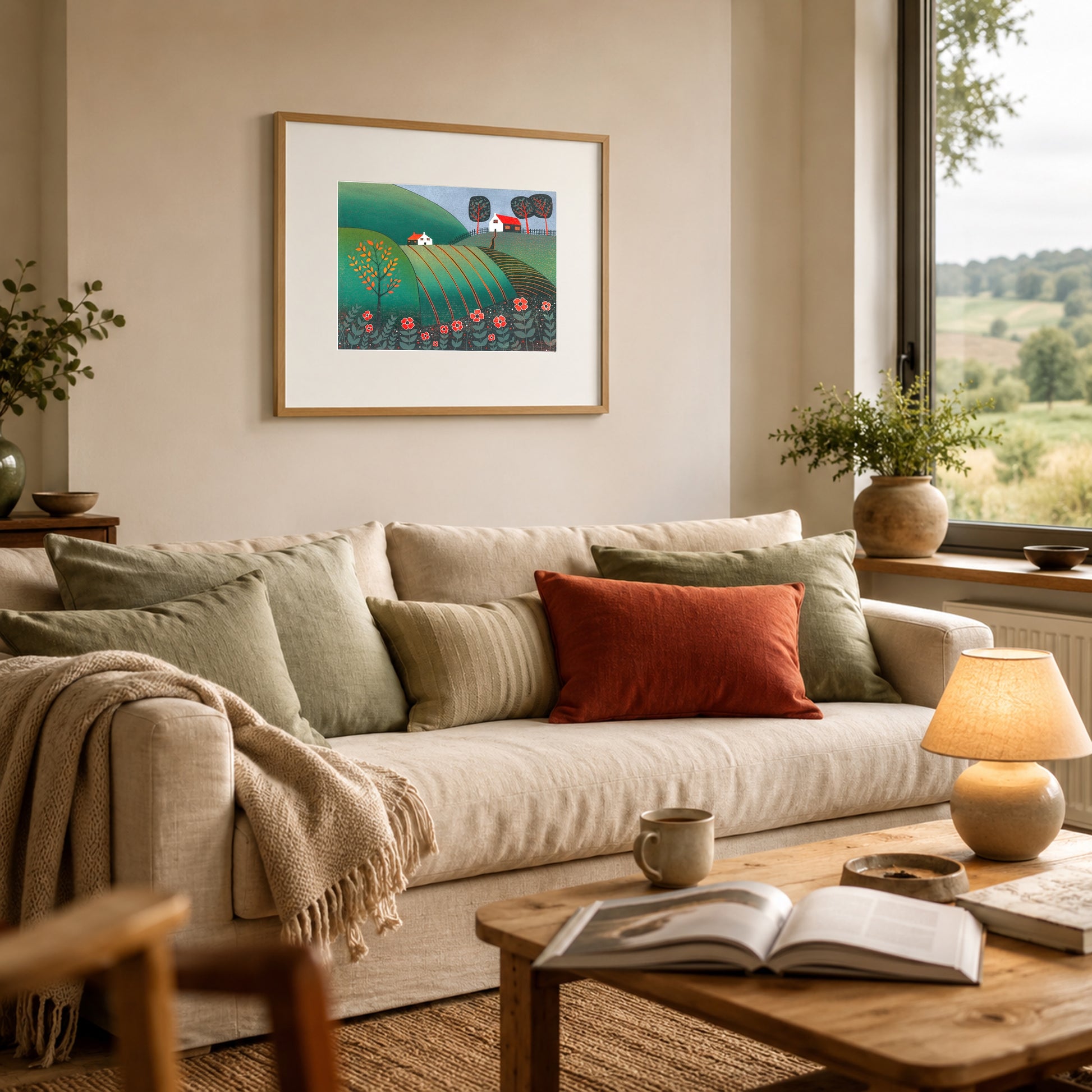 Framed green and red landscape print on a sage kitchen wall above a rustic oak table with wildflowers and bread.