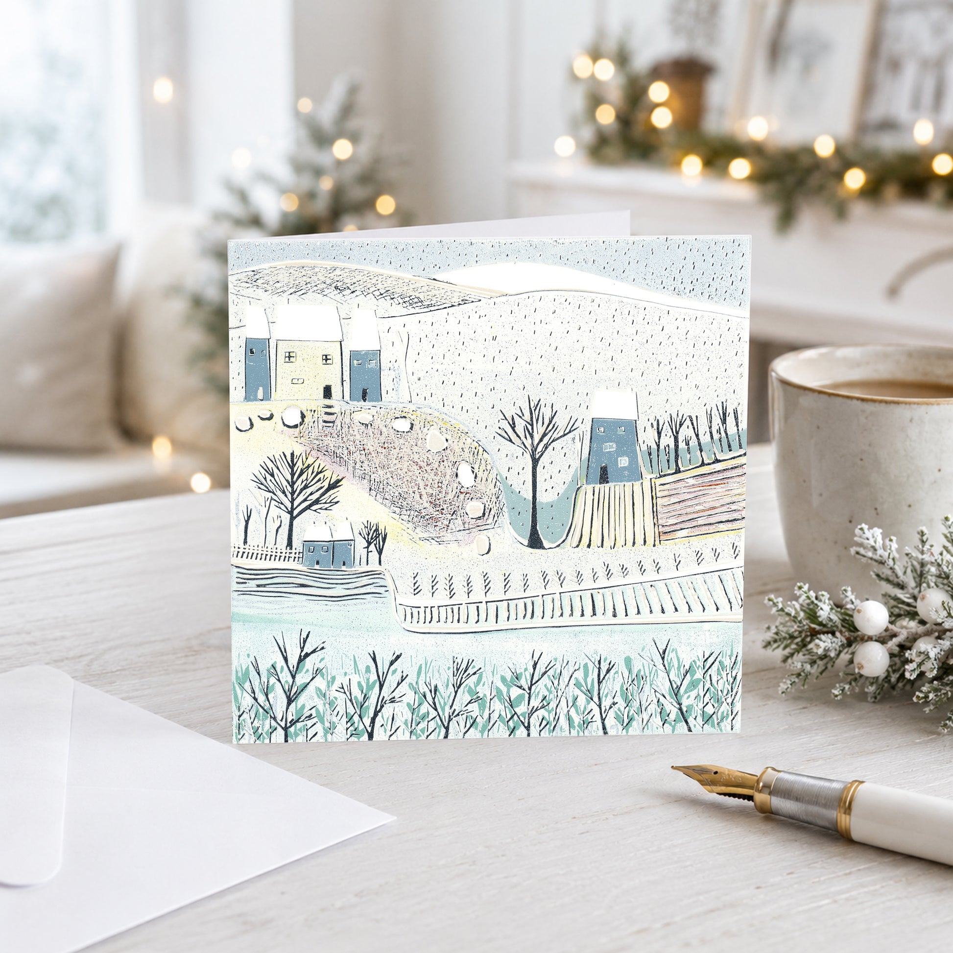 Winter landscape Christmas card with cottages and snowy fields displayed in a festive interior.