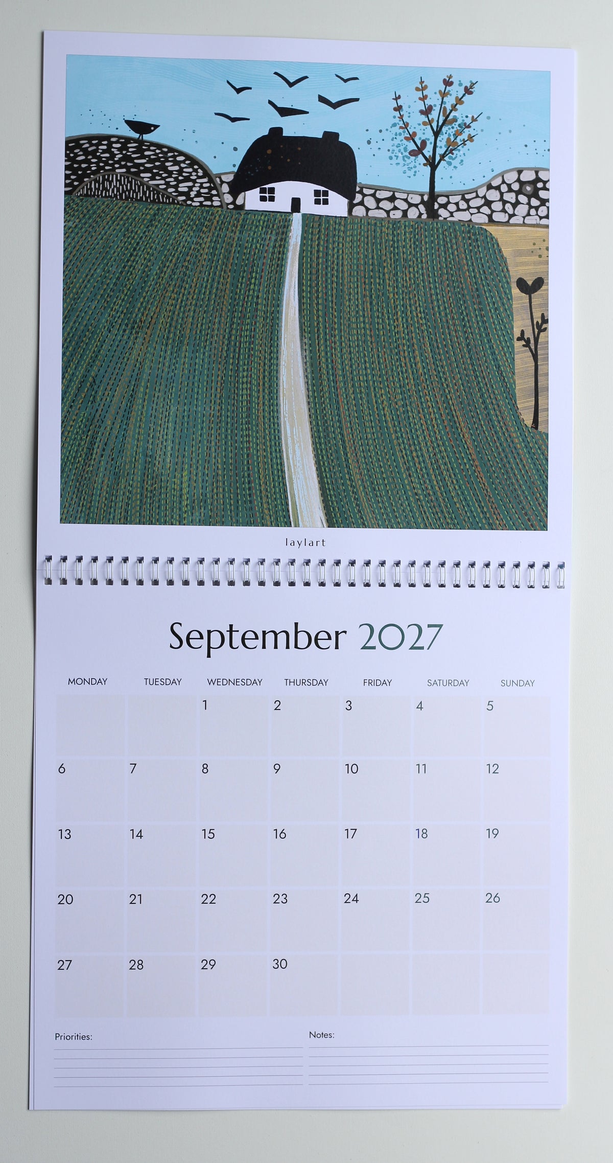 Photograph of the September 2027 square calendar showing green field artwork, monthly grid, priorities and notes.
