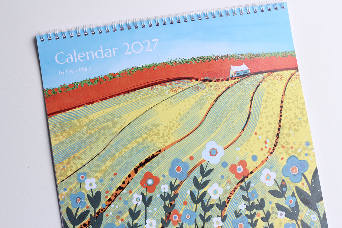 Photograph of the printed 20 x 20 cm 2027 calendar cover with yellow fields, flowers, spiral binding and hanging loop.