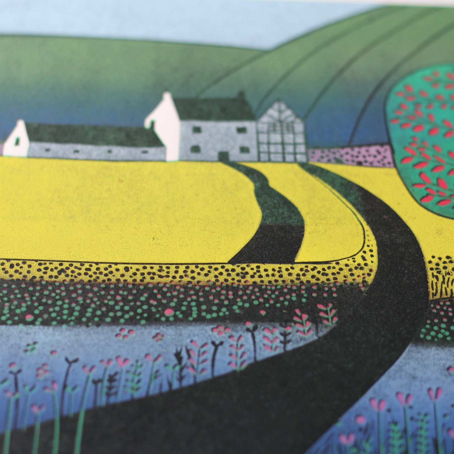 Close-up of the linocut showing the textured yellow field, green tree and hand-printed blue and violet wildflowers.
