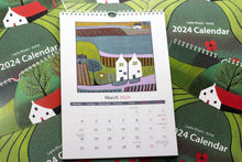 Load image into Gallery viewer, Open view of the 2024 Linocut Wall Calendar, showcasing the March 2024 page featuring a captivating linocut print of a rural landscape with charming houses, a creation by Laylart Studio.