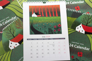 Open view of the 2024 Linocut Wall Calendar, unveiling the July page adorned with a vibrant linocut print portraying a colorful meadow of red and orange flowers, a backdrop of diverse trees, and a charming house, created by Laylart Studio.