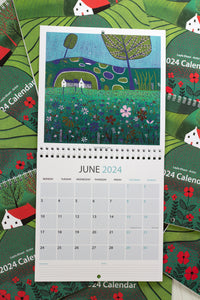 June 2024 Wall Art Calendar fully opened, featuring a colorful linocut print landscape. The image displays the date section and includes space for priorities and notes at the bottom.
