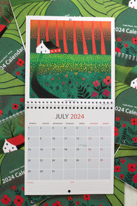 July 2024 calendar in 30 x 60 cm size, displaying an open view of the entire calendar, highlighting a stunning linocut print of a distant house framed by vibrant red and orange flowers in the foreground.