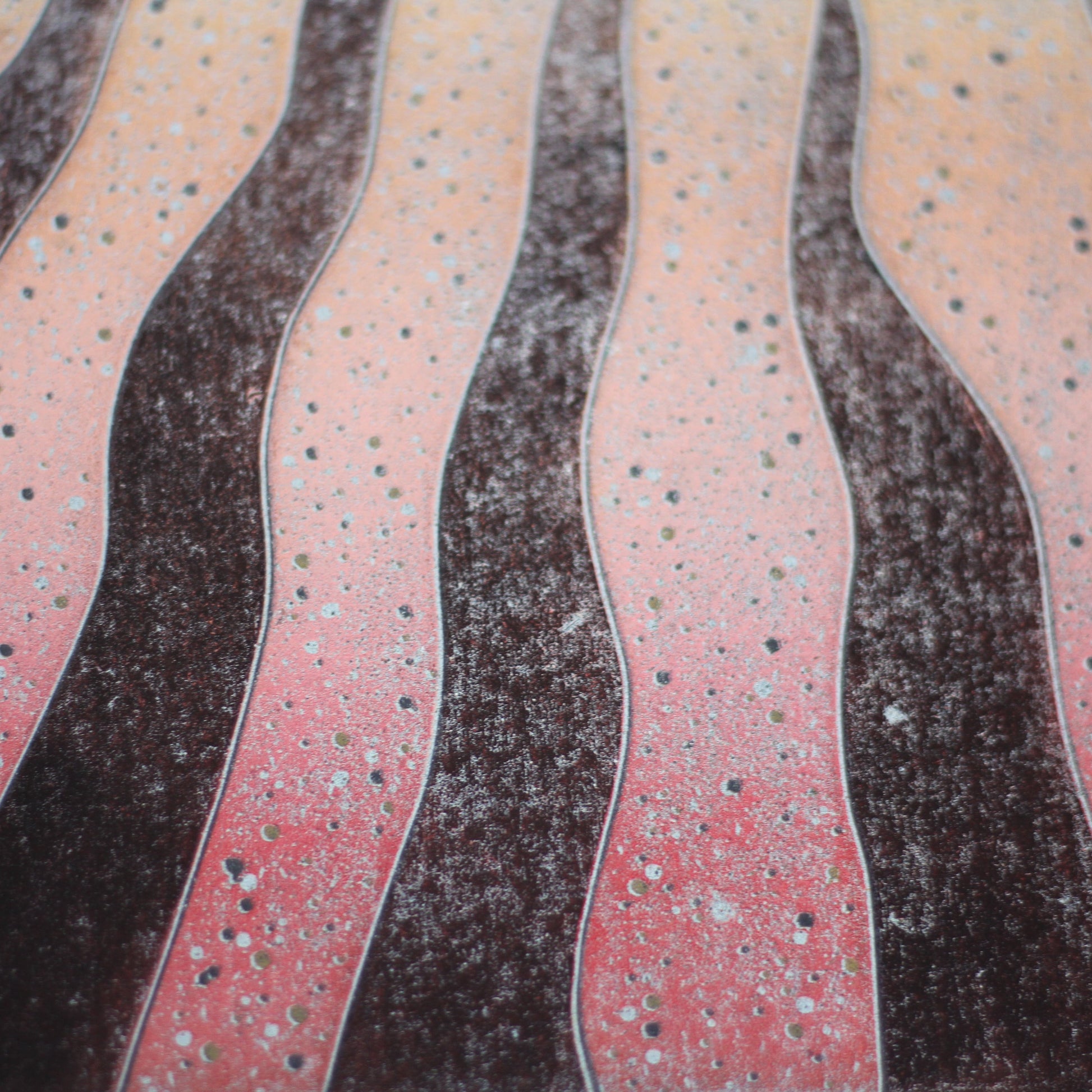 Close-up of the linocut showing the textured red and charcoal furrows hand-printed with gold and silver speckling.