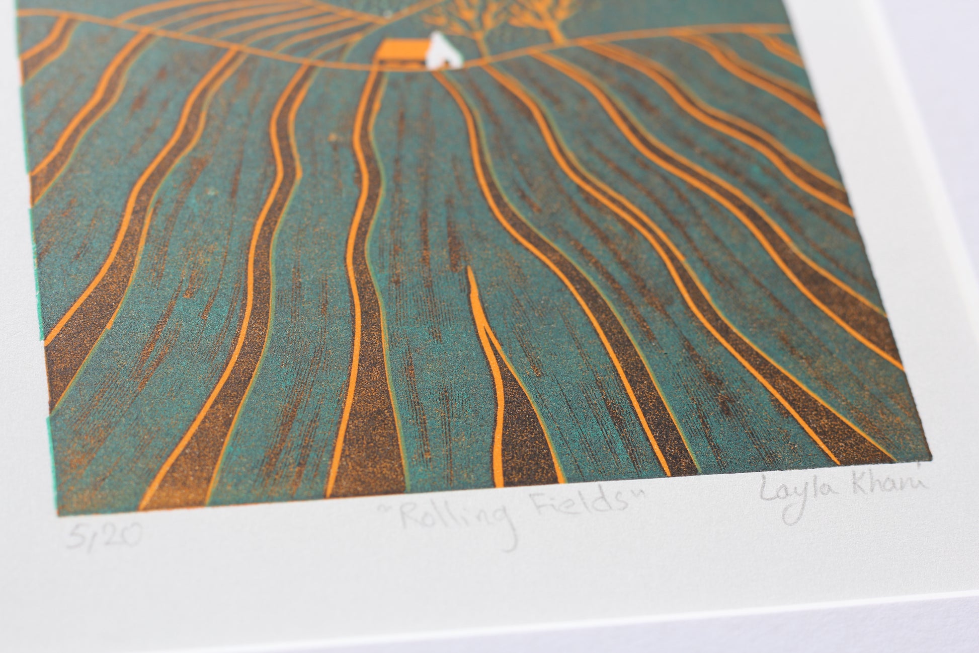 Close angled view of an original mini linocut print, orange furrows across green hills