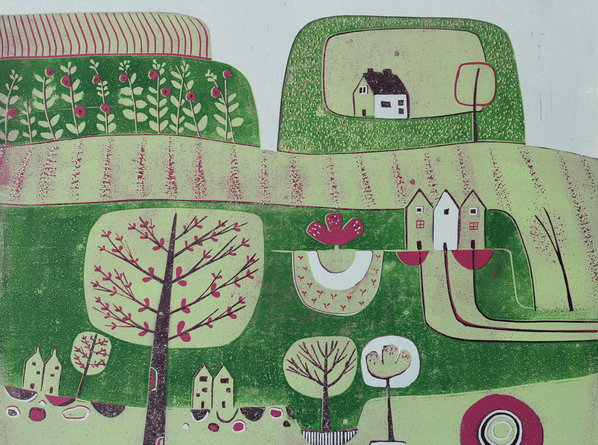 A close up of a stylized folk-art landscape linocut print featuring green hills, white houses, and trees with pink blossoms, shown against a light blue background.