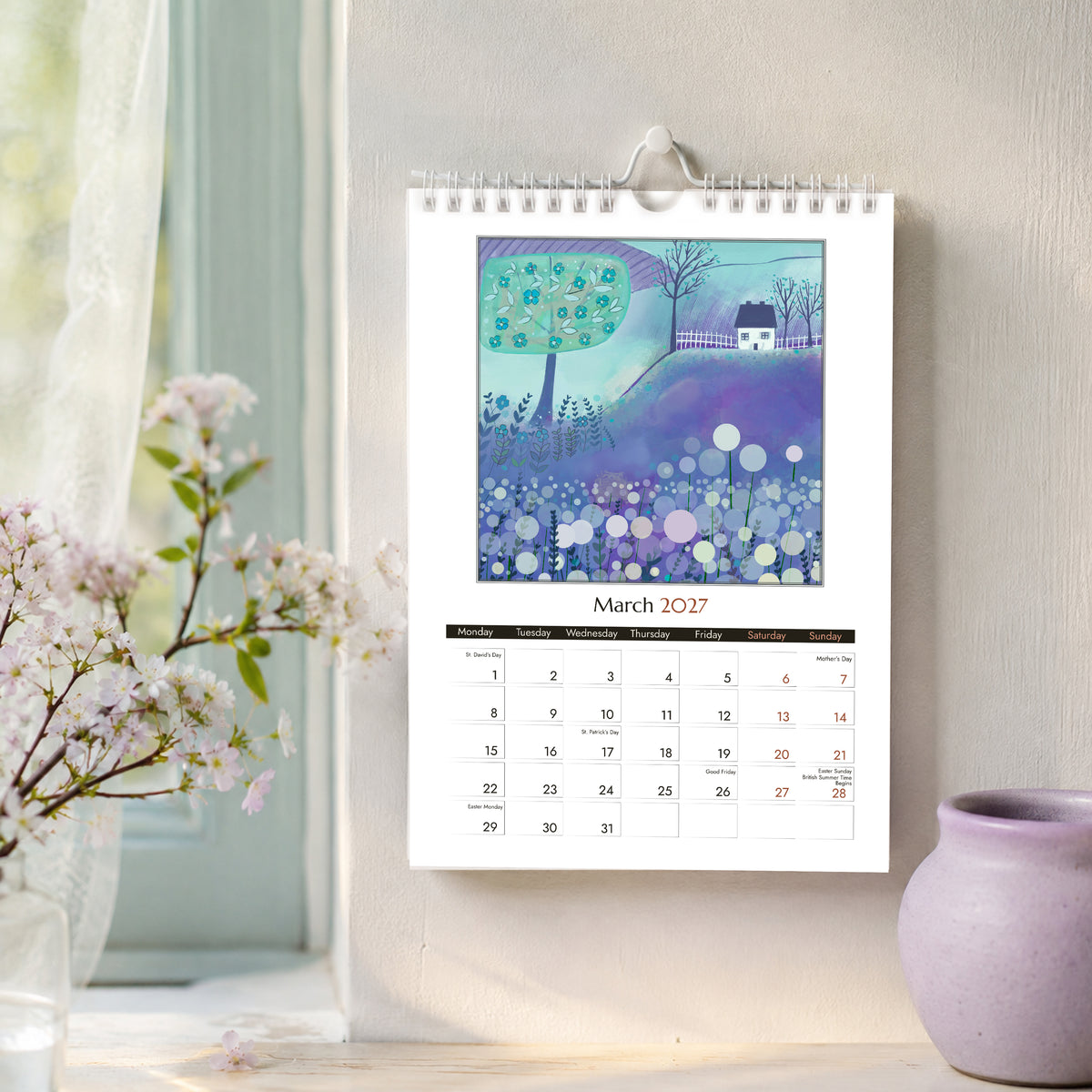 March 2027 A4 art wall calendar with blue and lavender spring landscape, styled beside blossom and a lilac ceramic vase.