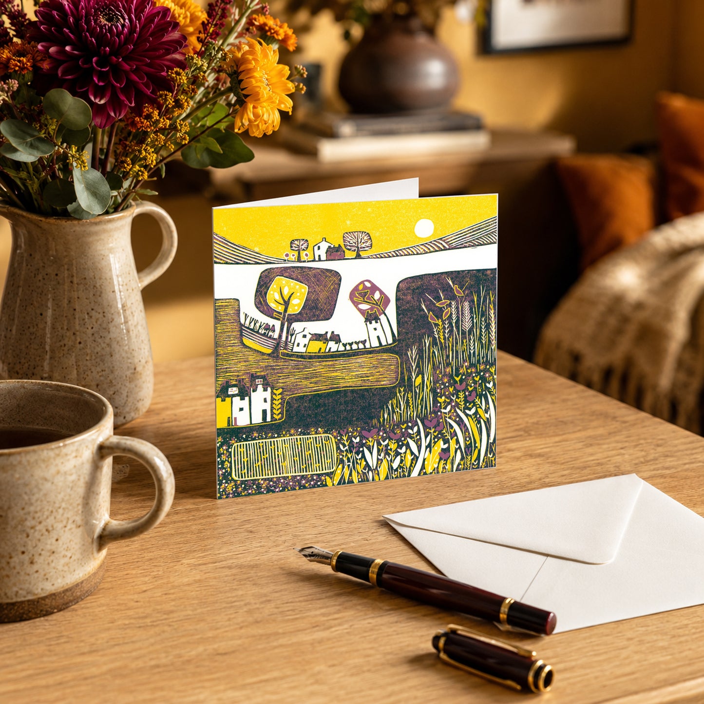 Linocut autumn greeting card standing on a table with a stone jug and dahlias