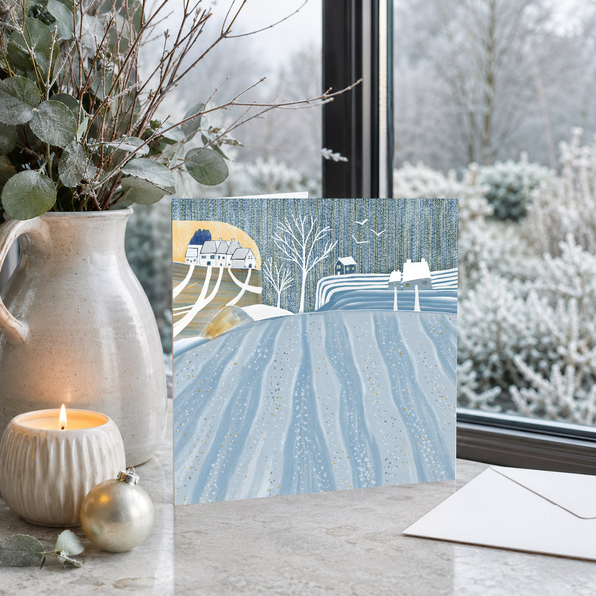 Fields Under Snow Christmas greeting card displayed beside a snowy window
