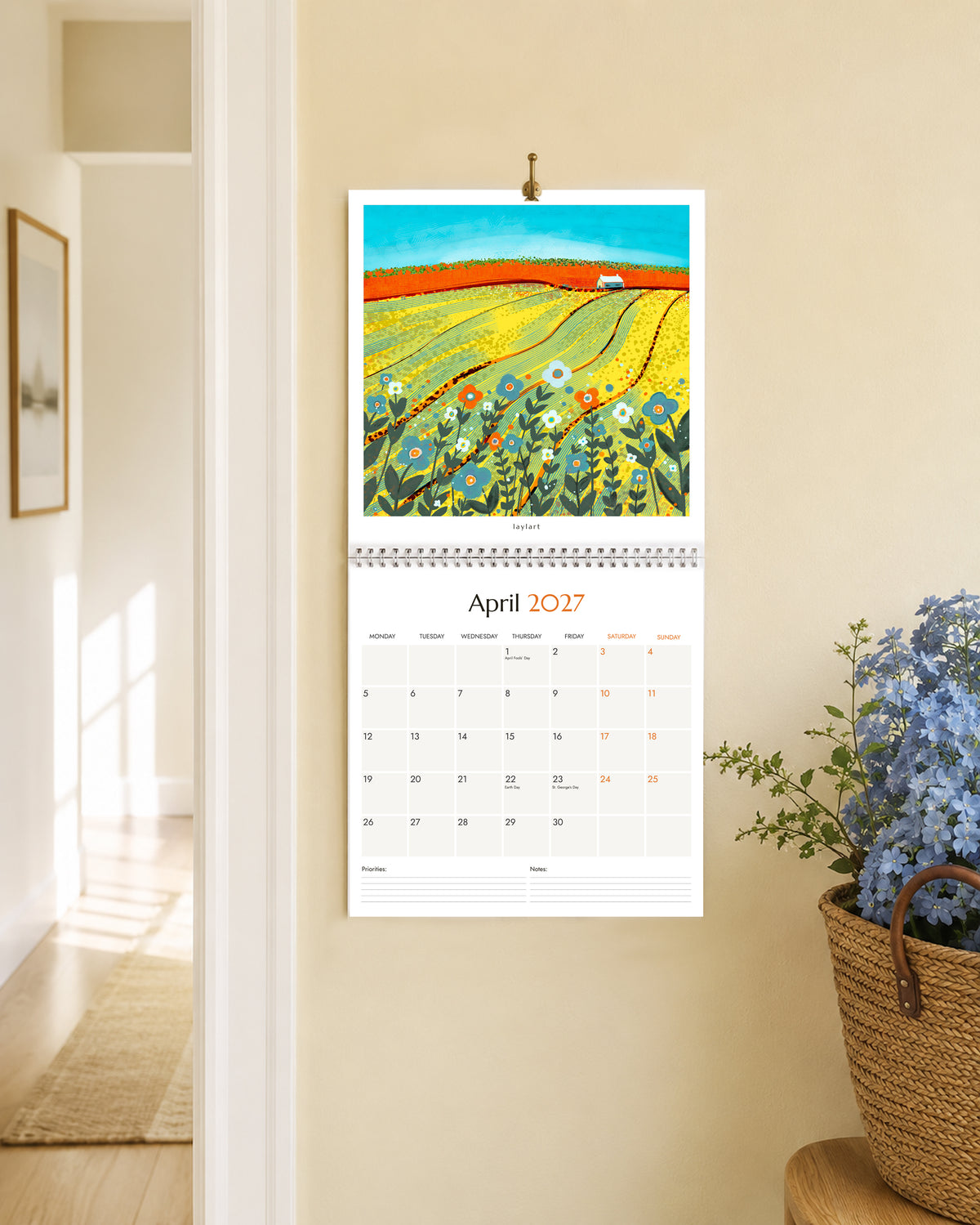 Large 2027 wall calendar open to April with colourful yellow field landscape painting
