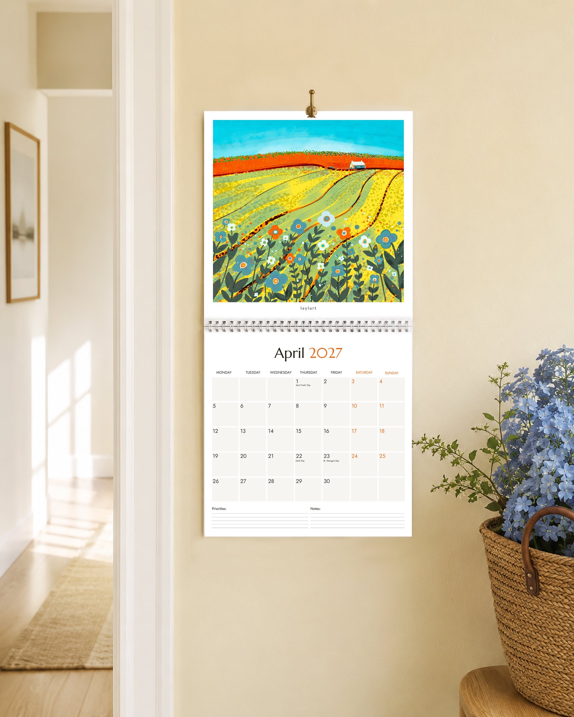 Large 2027 wall calendar open to April with colourful yellow field landscape painting