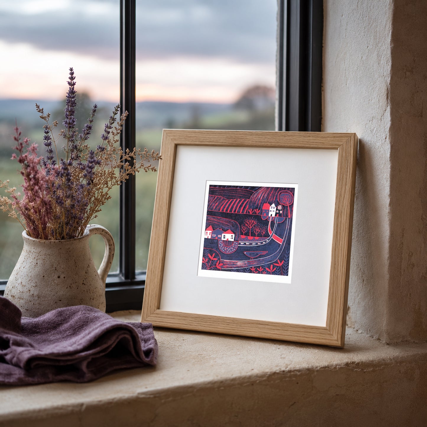 Mini linocut print framed in pale oak, propped on a windowsill with heather in a stone jug