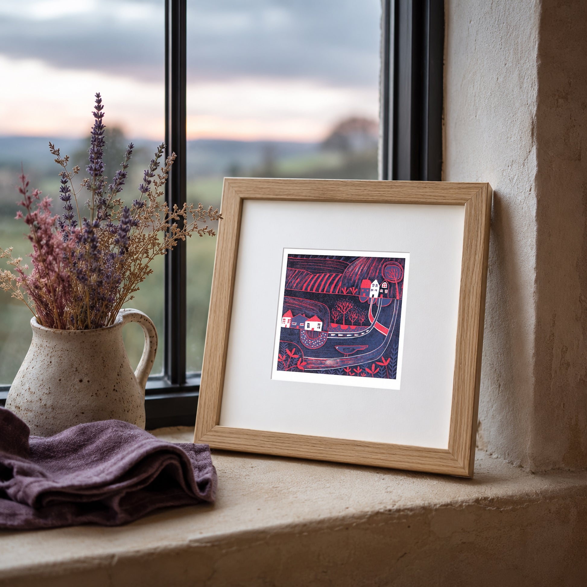 Mini linocut print framed in pale oak, propped on a windowsill with heather in a stone jug