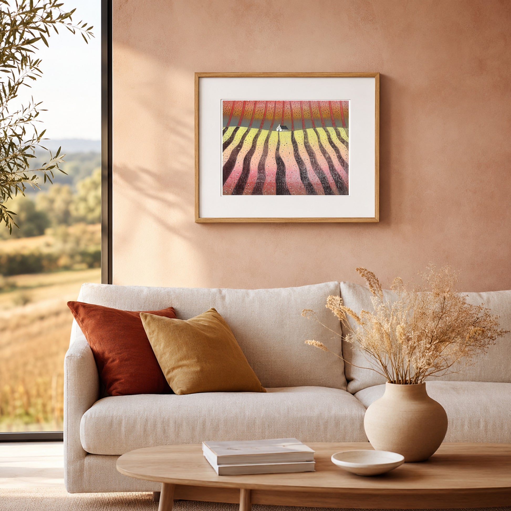 Framed print of a red and gold landscape on a warm terracotta wall above a cream sofa with a rust cushion.