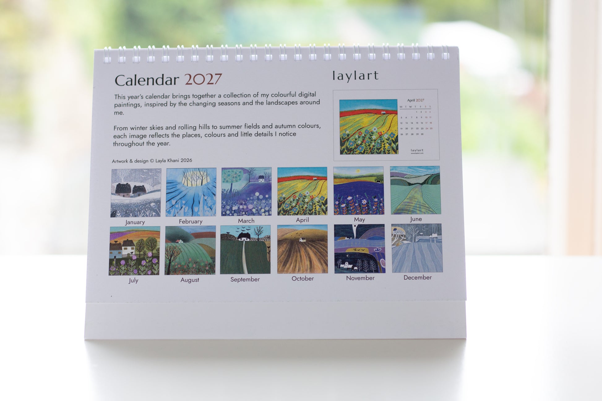Photograph of the back of the printed 2027 desk calendar showing the collection of 12 seasonal artworks and product details.