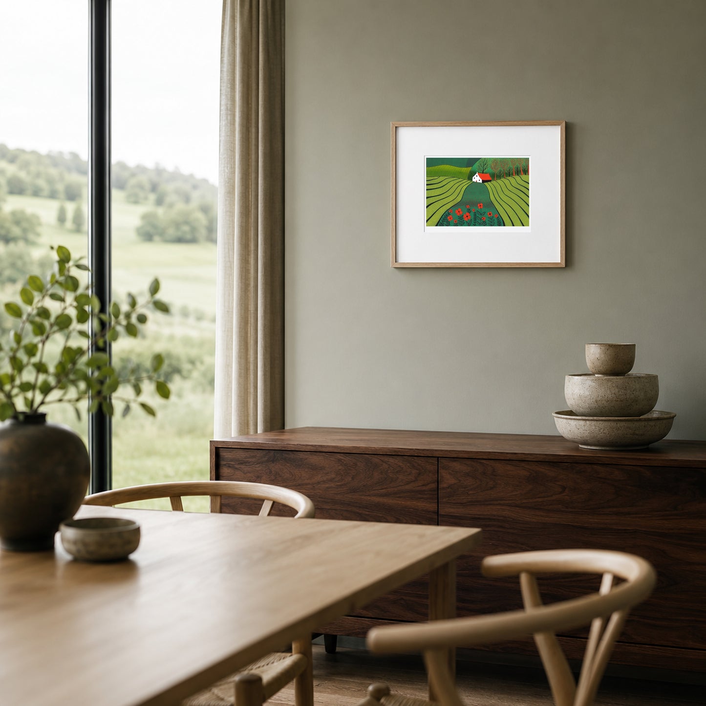 Framed green and red landscape print on a sage-grey wall above a walnut sideboard in a contemporary dining nook.