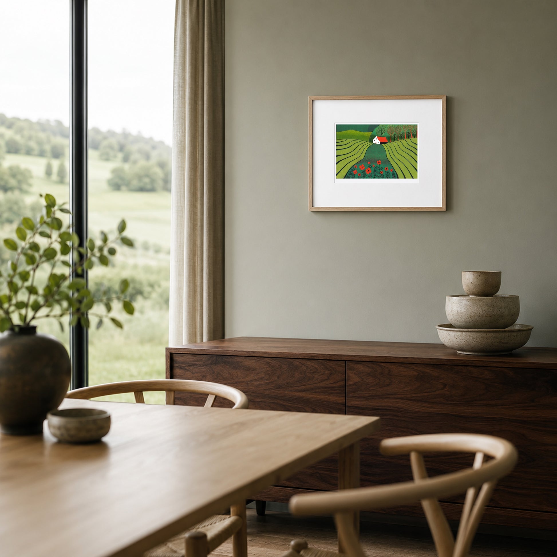 Framed green and red landscape print on a sage-grey wall above a walnut sideboard in a contemporary dining nook.