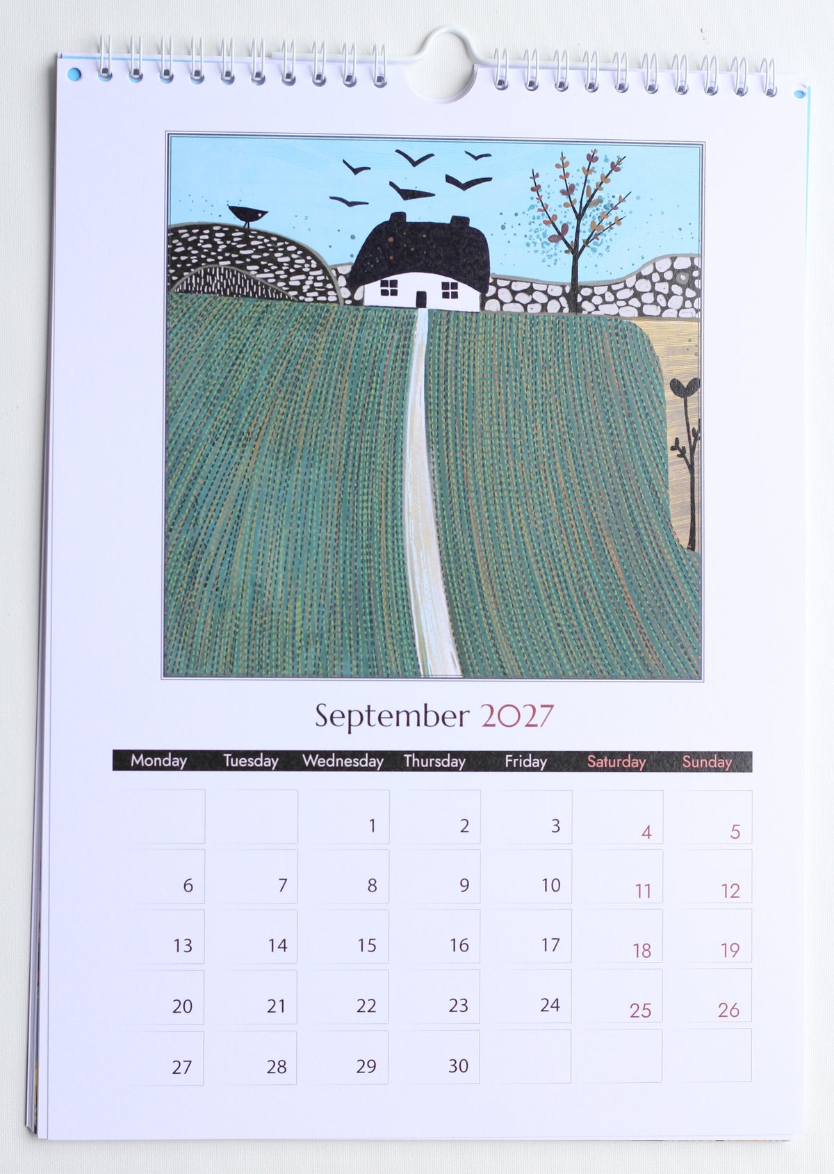 Photograph of the September 2027 printed calendar page showing green field artwork, monthly grid and spiral binding.