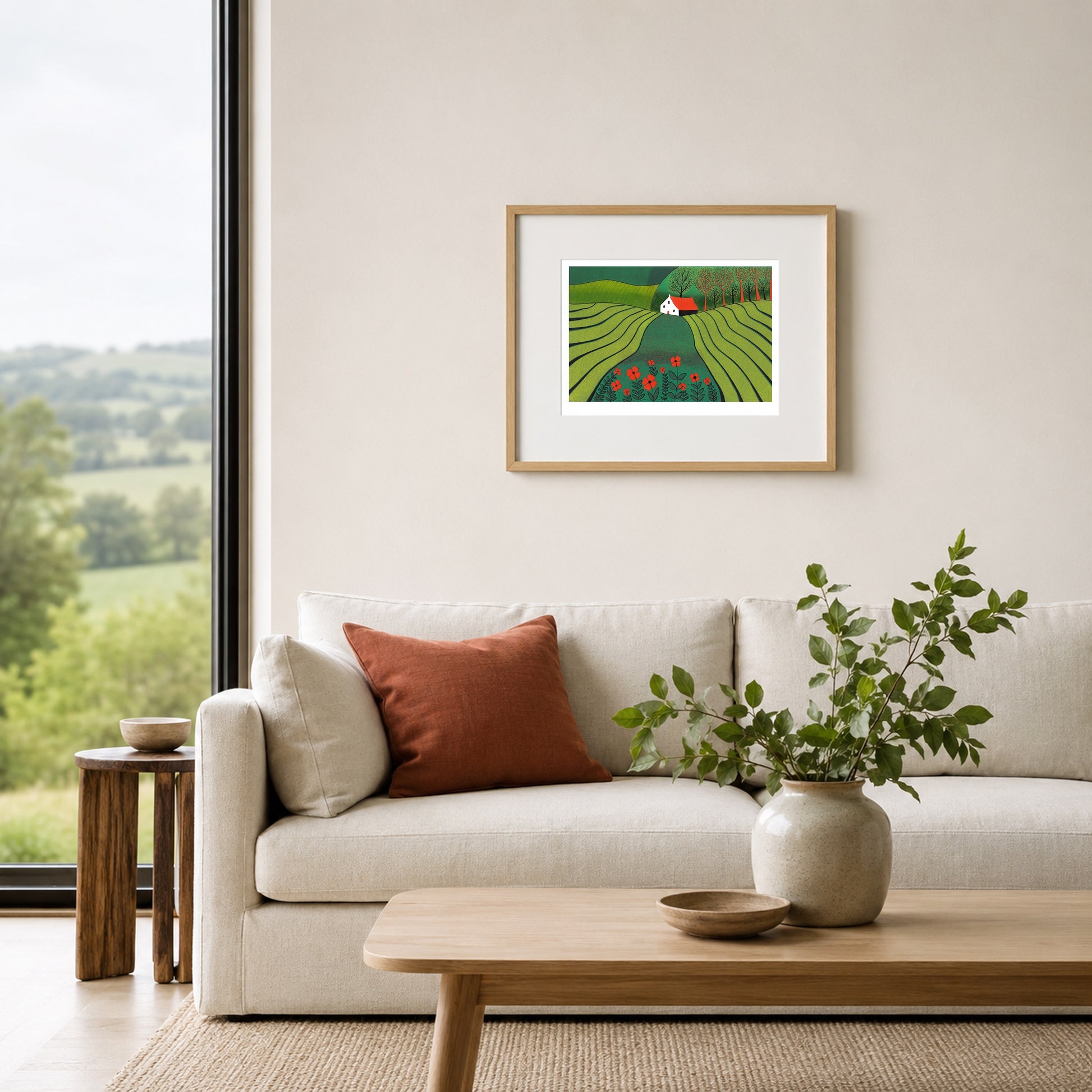 Framed linocut of a green poppy landscape on a warm white bedroom wall above an oatmeal upholstered headboard.