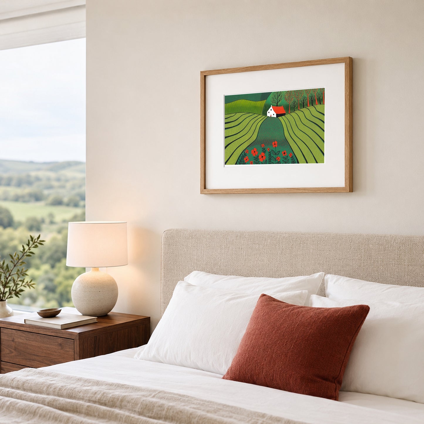 Framed linocut of a green poppy landscape on a warm white bedroom wall above an oatmeal upholstered headboard.