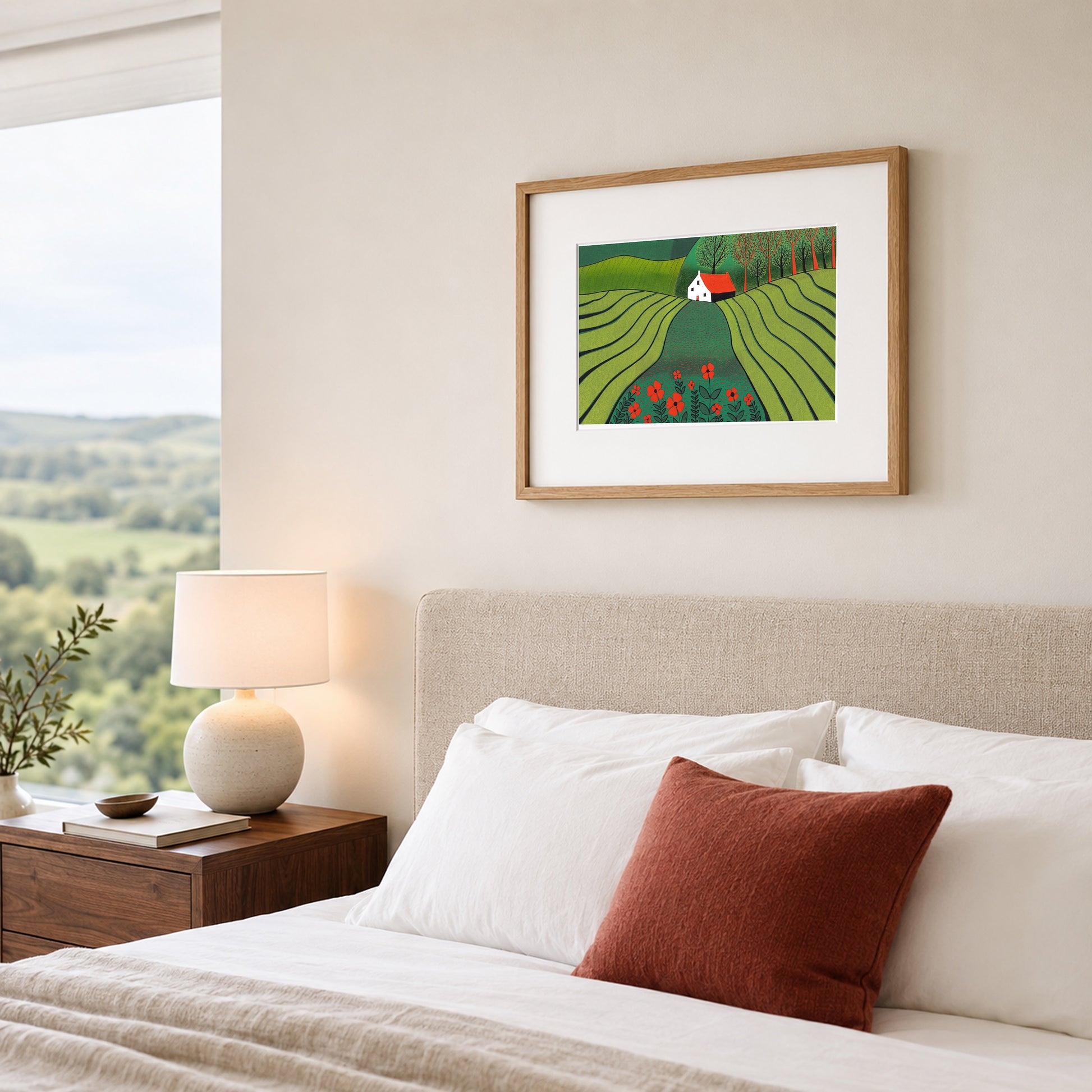 Framed linocut of a green poppy landscape on a warm white bedroom wall above an oatmeal upholstered headboard.