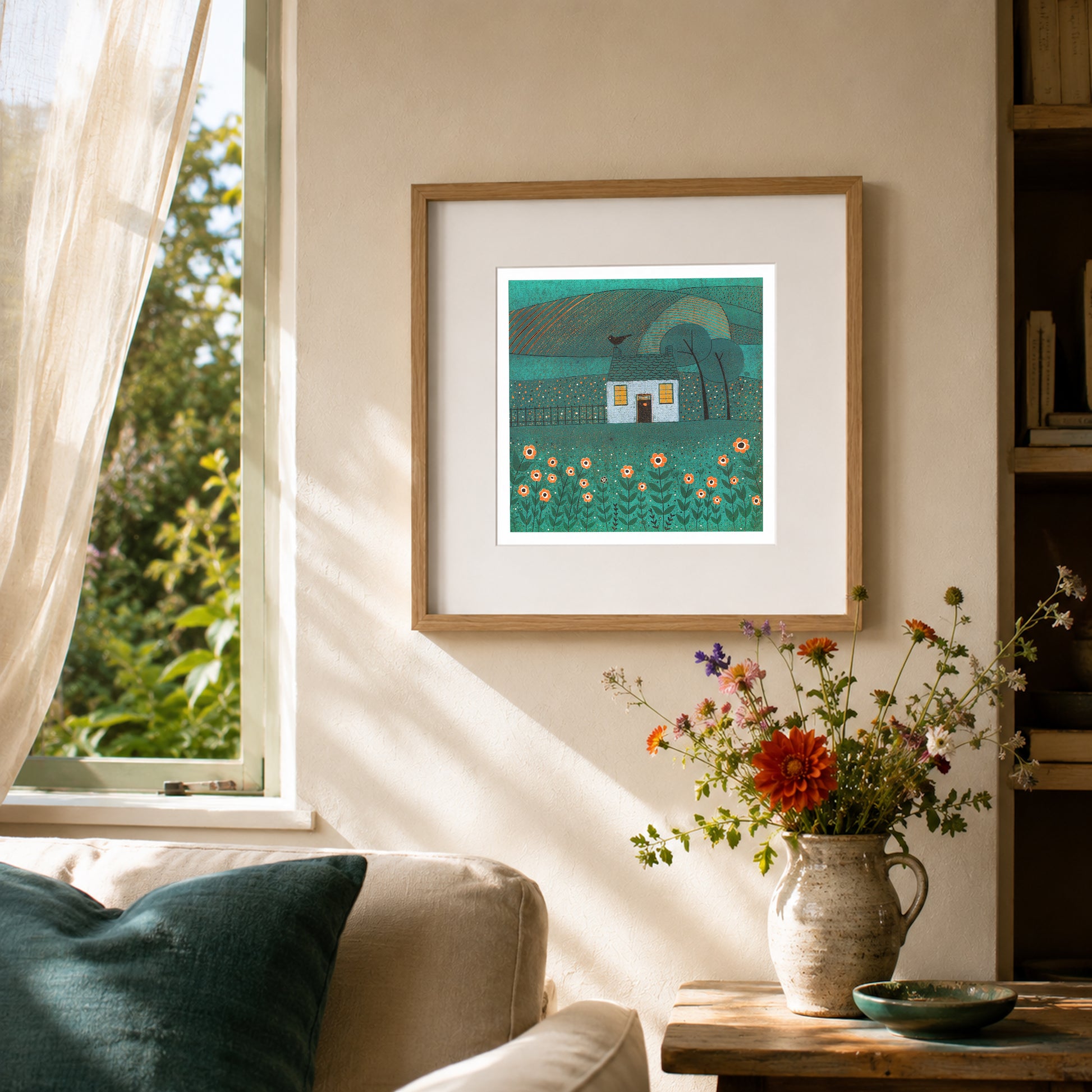Framed The House with the Bird linocut print displayed beside an open window in a warm sitting room with flowers.