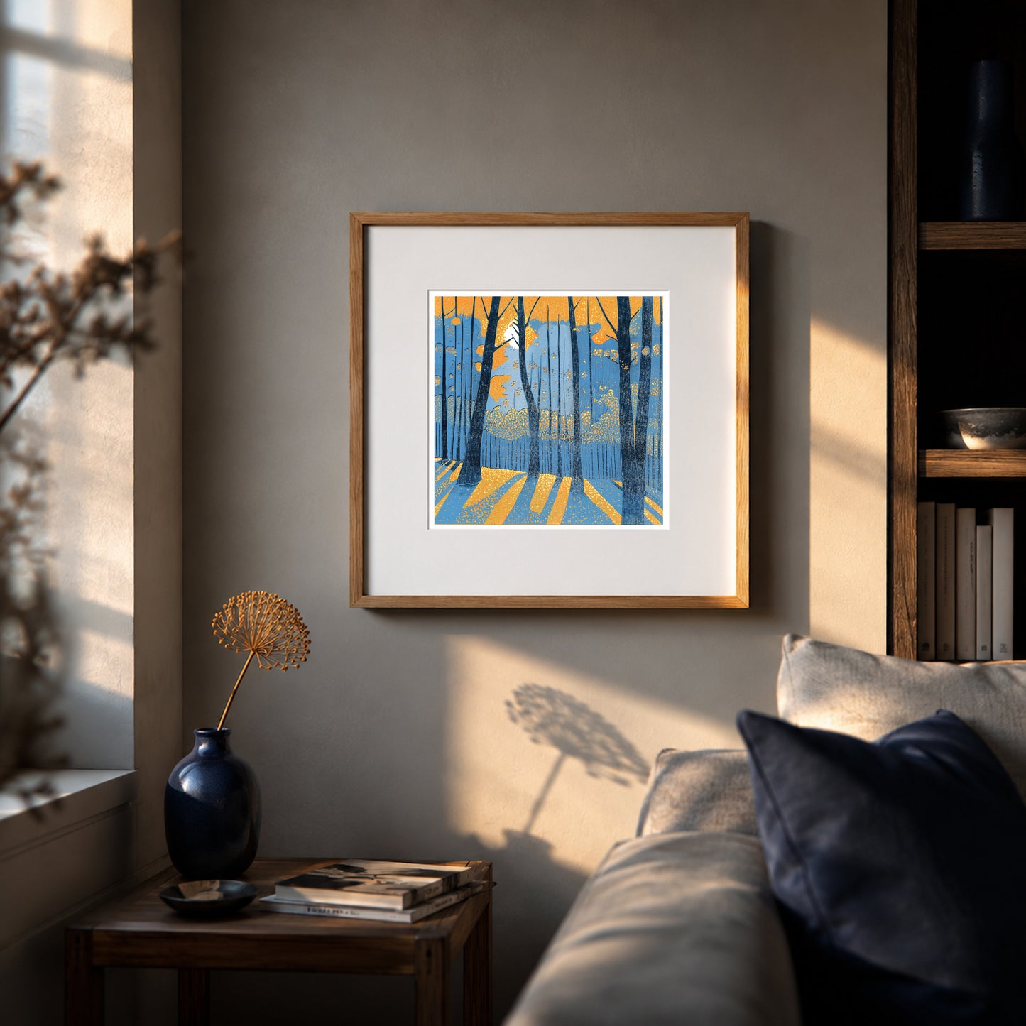 Framed Into the Woodland linocut print displayed above a sofa in a warm interior with evening sunlight and dark blue accents.
