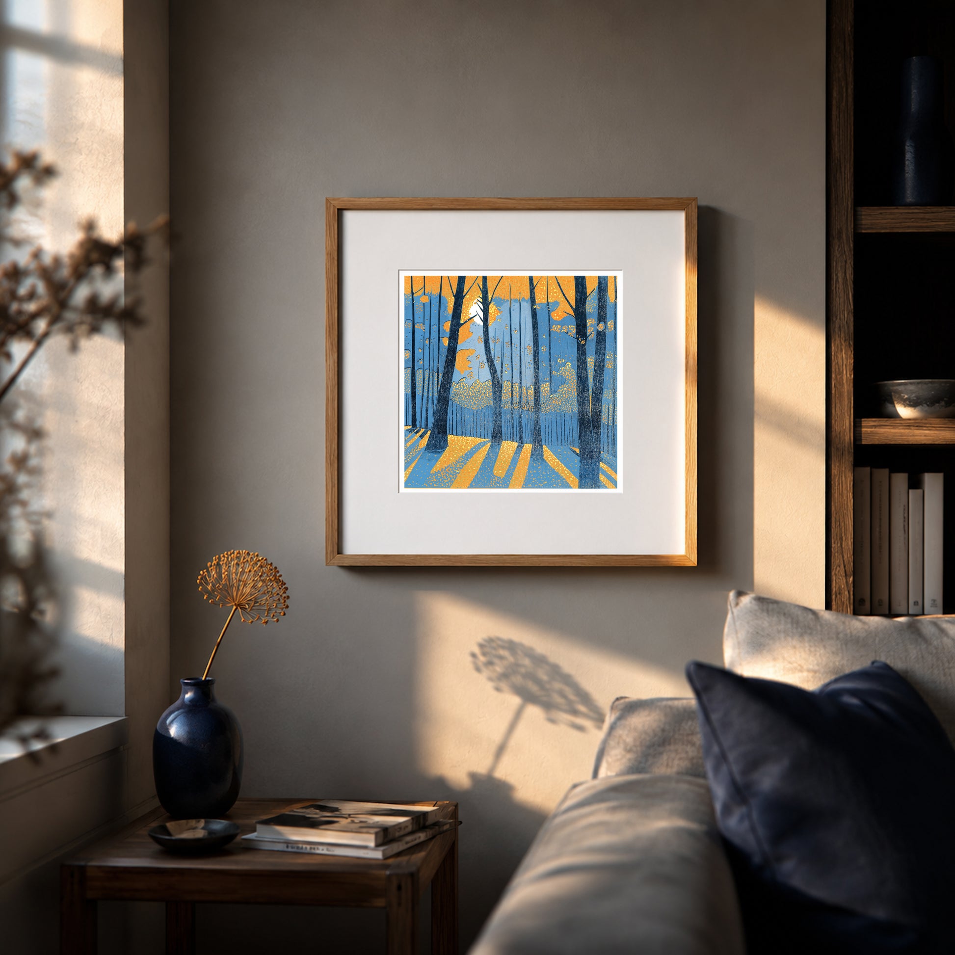 Framed Into the Woodland linocut print displayed above a sofa in a warm interior with evening sunlight and dark blue accents.
