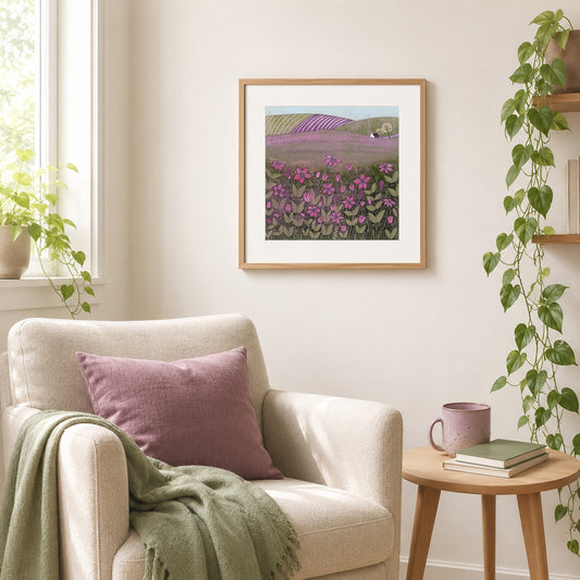 Purple meadow linocut print framed in oak above a cream armchair with a mauve cushion and sage throw.