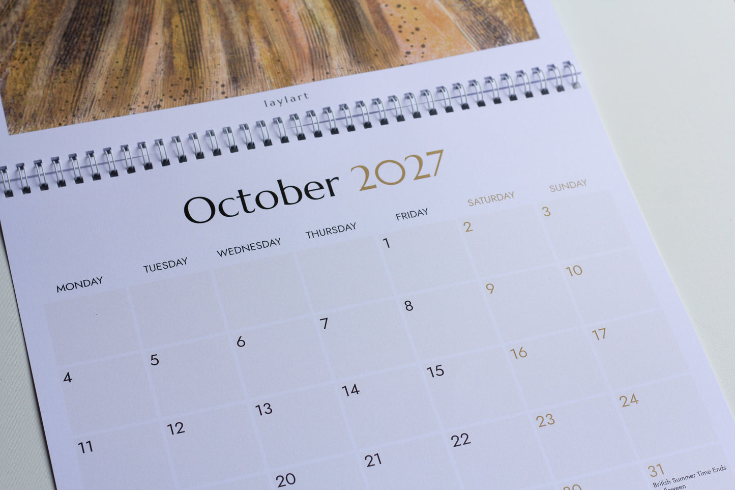 Close-up photograph of the October 2027 printed calendar showing spiral binding, autumn artwork and monthly planning grid.