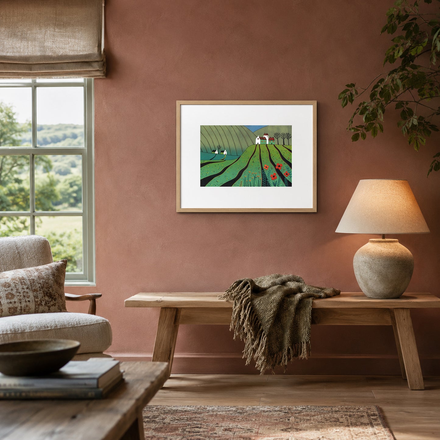 Framed poppy landscape print on a soft terracotta wall above a light oak bench with a wool throw and lamp.