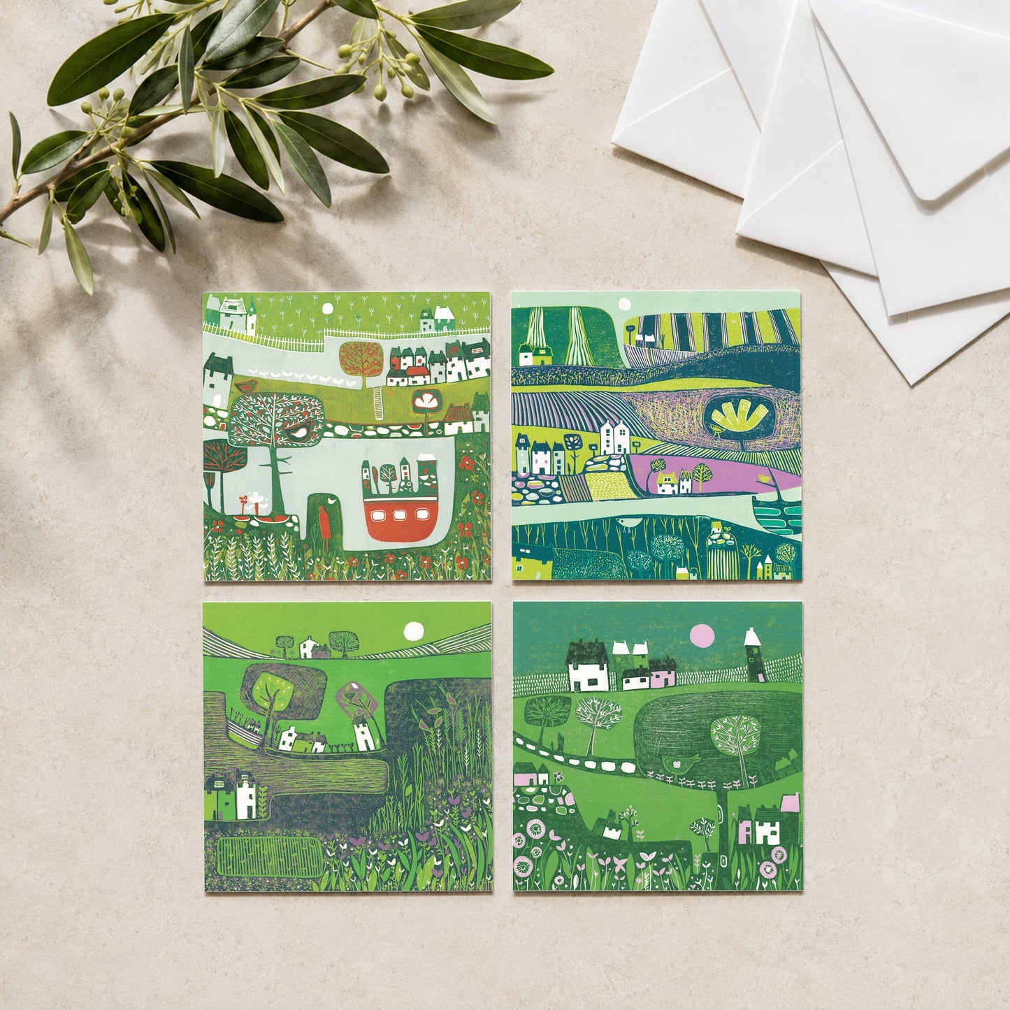 Set of four green linocut greeting cards of countryside scenes, styled with olive branches and envelopes, by Layla Khani